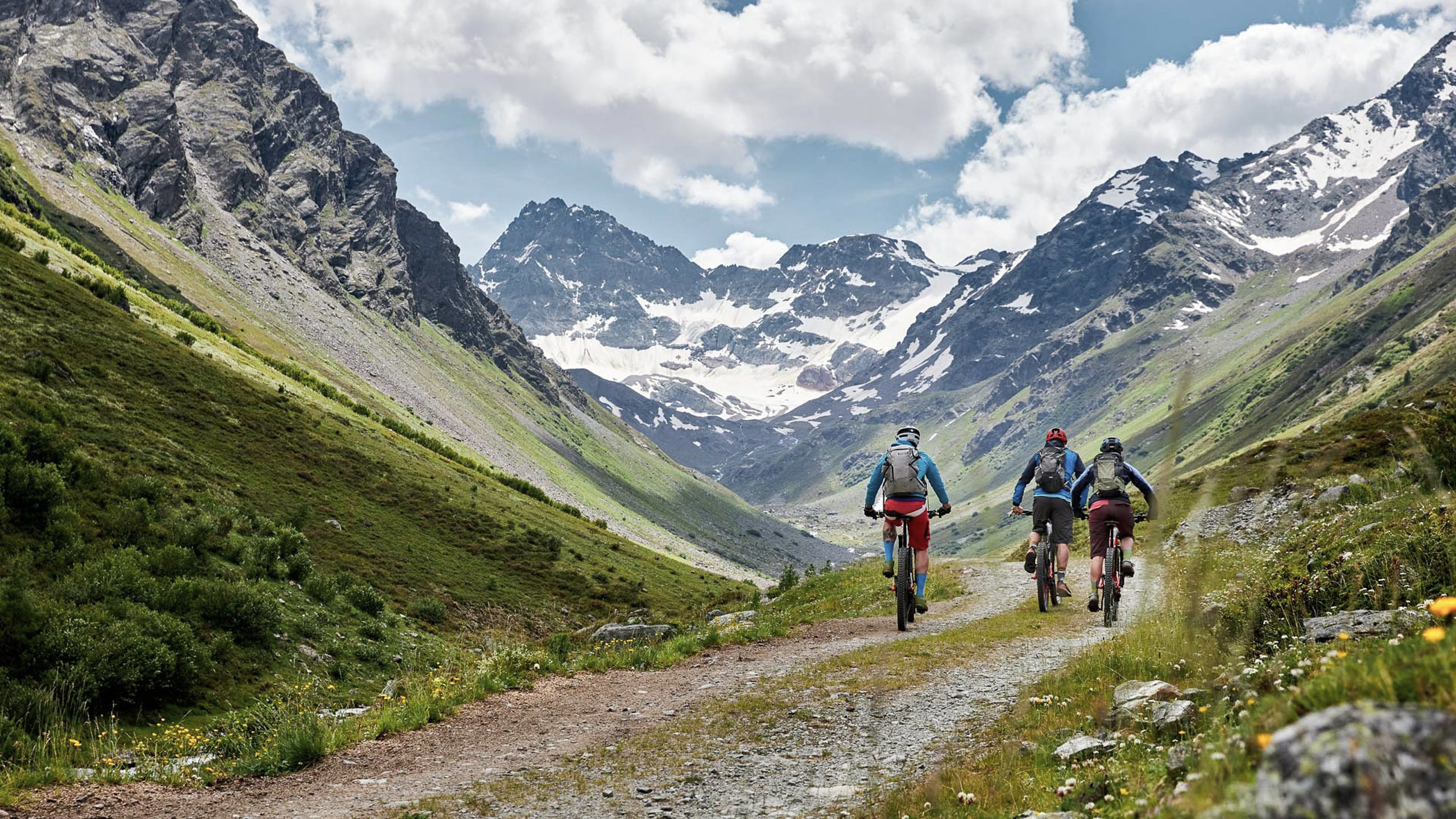 Die Bilder aus dem Hotel Salnerhof Drei Radfahrer fahren auf einem Bergweg mit schneebedeckten Gipfeln im Hintergrund