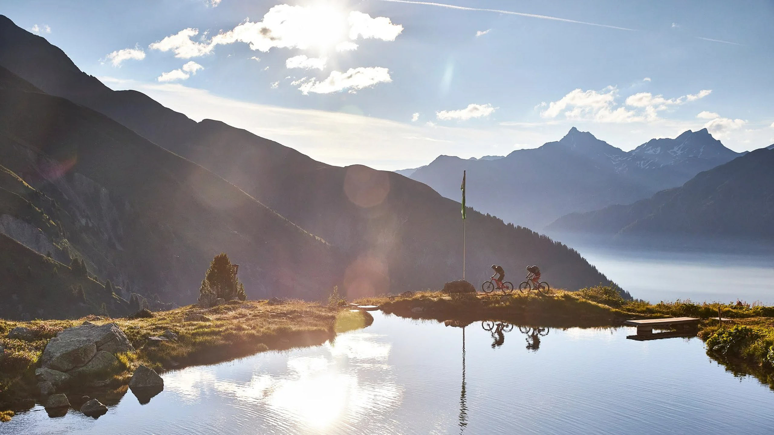 Die Bilder aus dem Hotel Salnerhof Zwei Radfahrer fahren entlang eines Bergsees bei Sonnenuntergang mit Bergen im Hintergrund