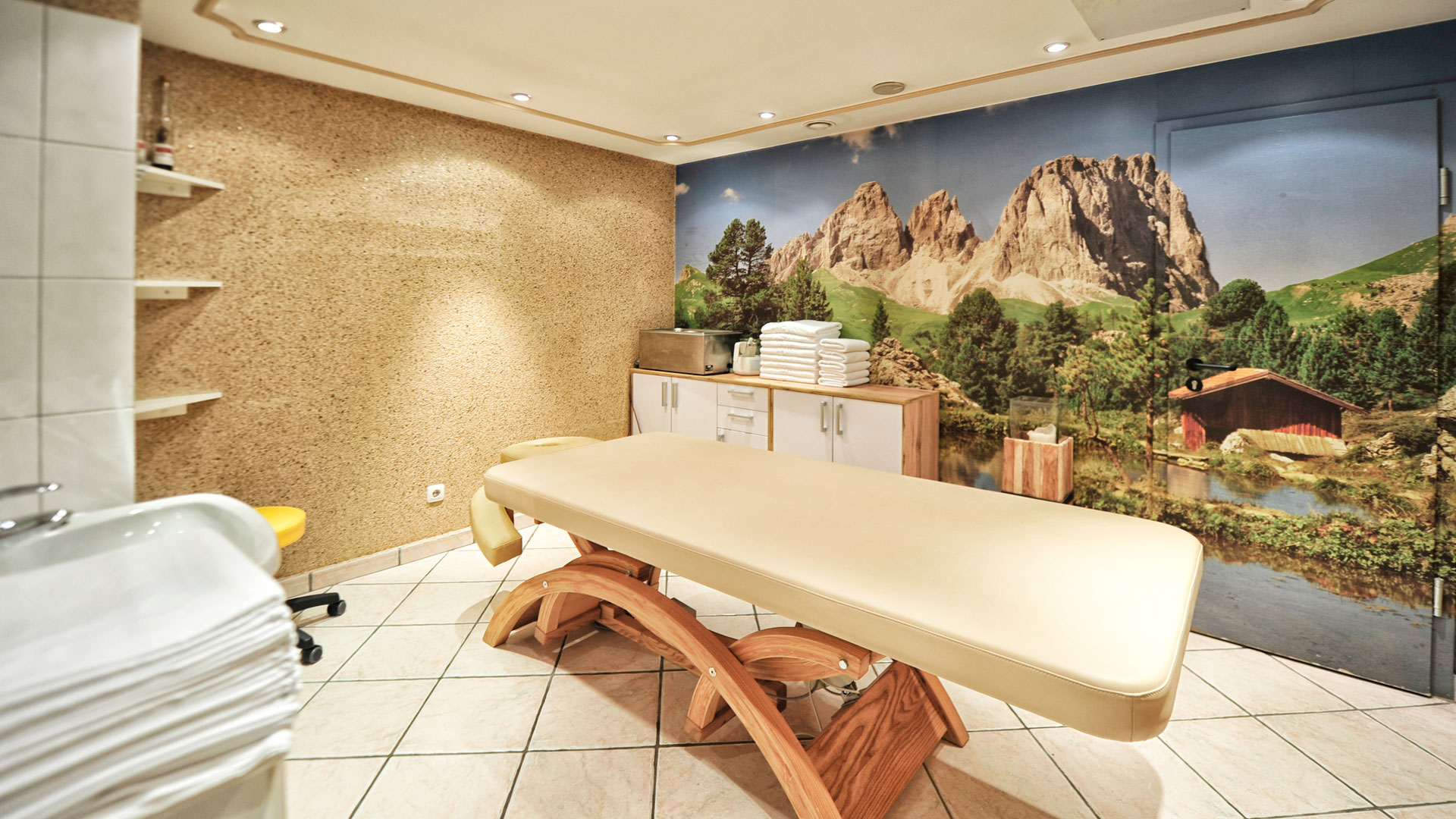 Heller Massageraum mit Alpenpanorama-Wandbild, Liege und Handtüchern im Hotel Salnerhof.