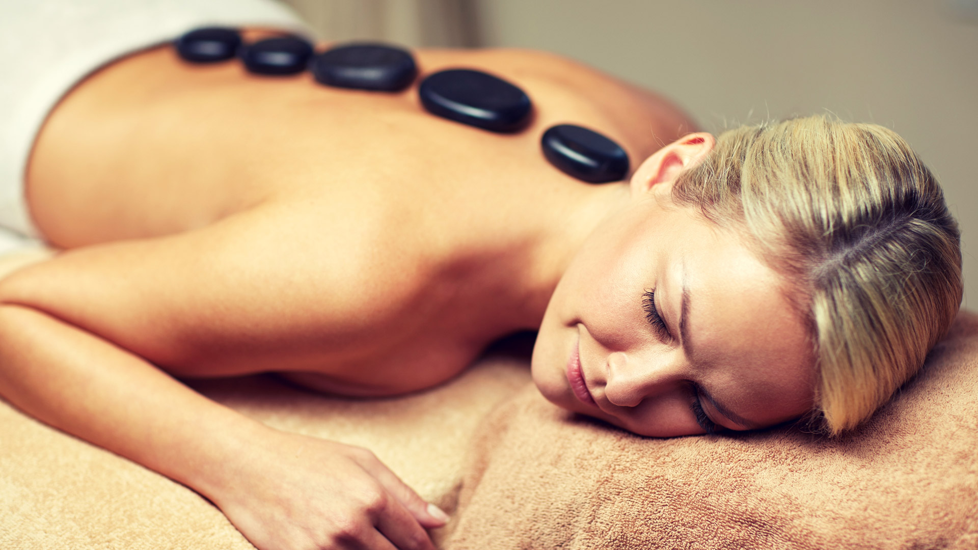 Frau liegt entspannt mit heißen Steinen auf dem Rücken bei einer Hot-Stone-Massage
